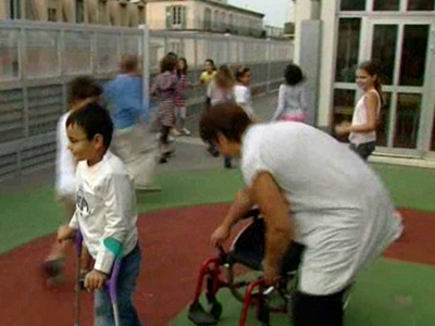 Une auxiliaire de vie scolaire dans la cour d'une école avec un jeune garçon en fauteuil dans les alpes maritimes en septembre 2011