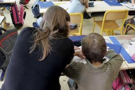 une jeune femme au coté d'un enfant dans un classe parisienne au titre de l'accompagnement de vie scolaire 