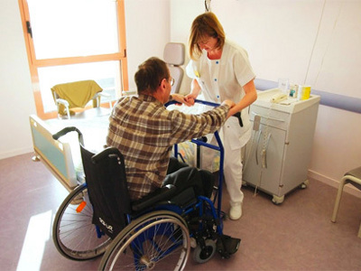 une personne âgée en perte autonomie dans un fauteuil avec une aide soignante pour l'aider dans les gestes quotidiens. Photo d'illustration 